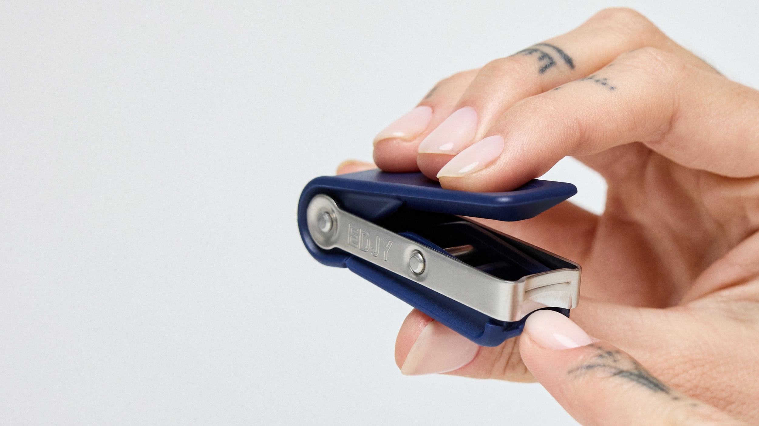A person with tattooed fingers using a navy EDJY Fingernail Cutter to trim their fingernails.
