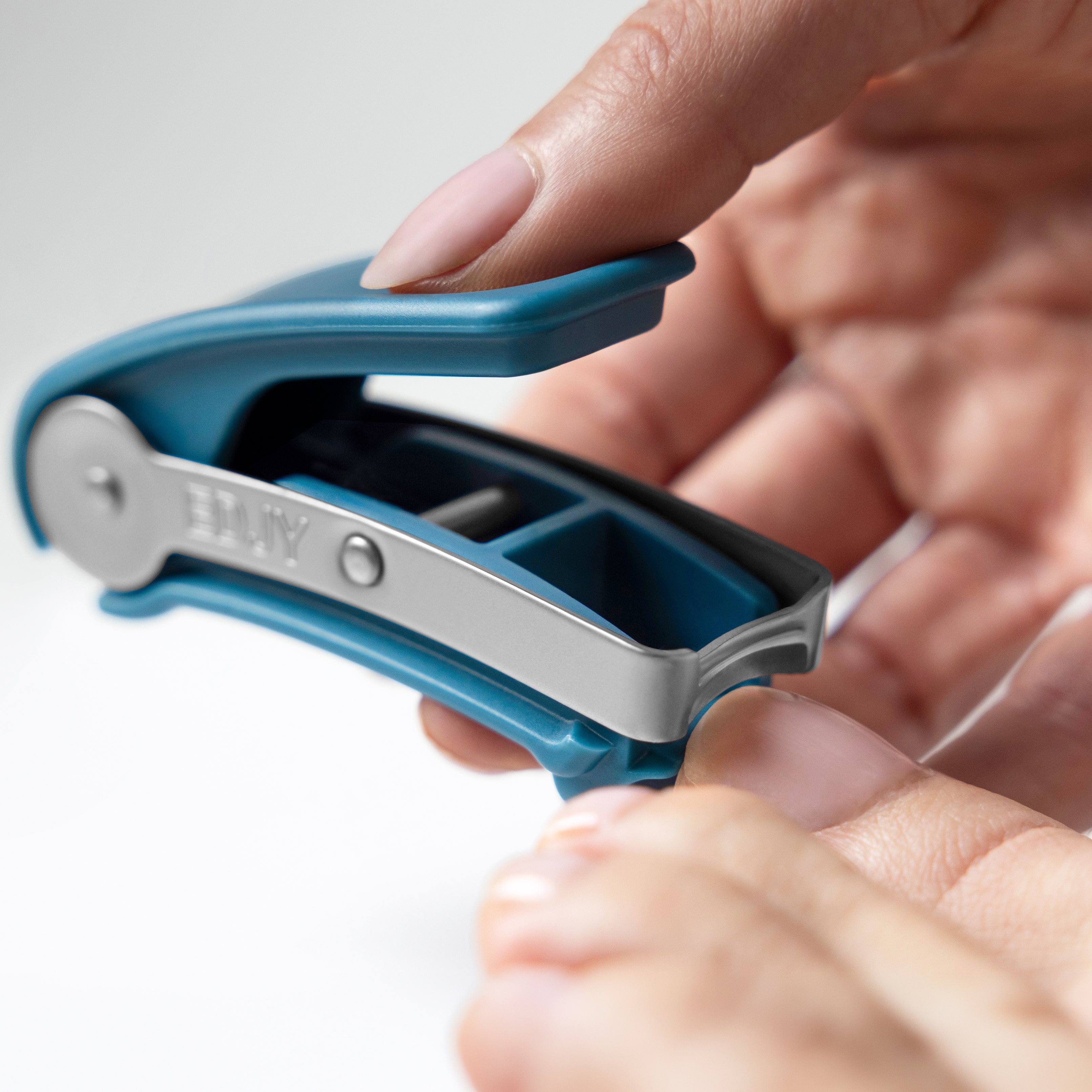 Close-up view of a hand holding and operating a teal EDJY Toenail Cutter to trim their toenail.  